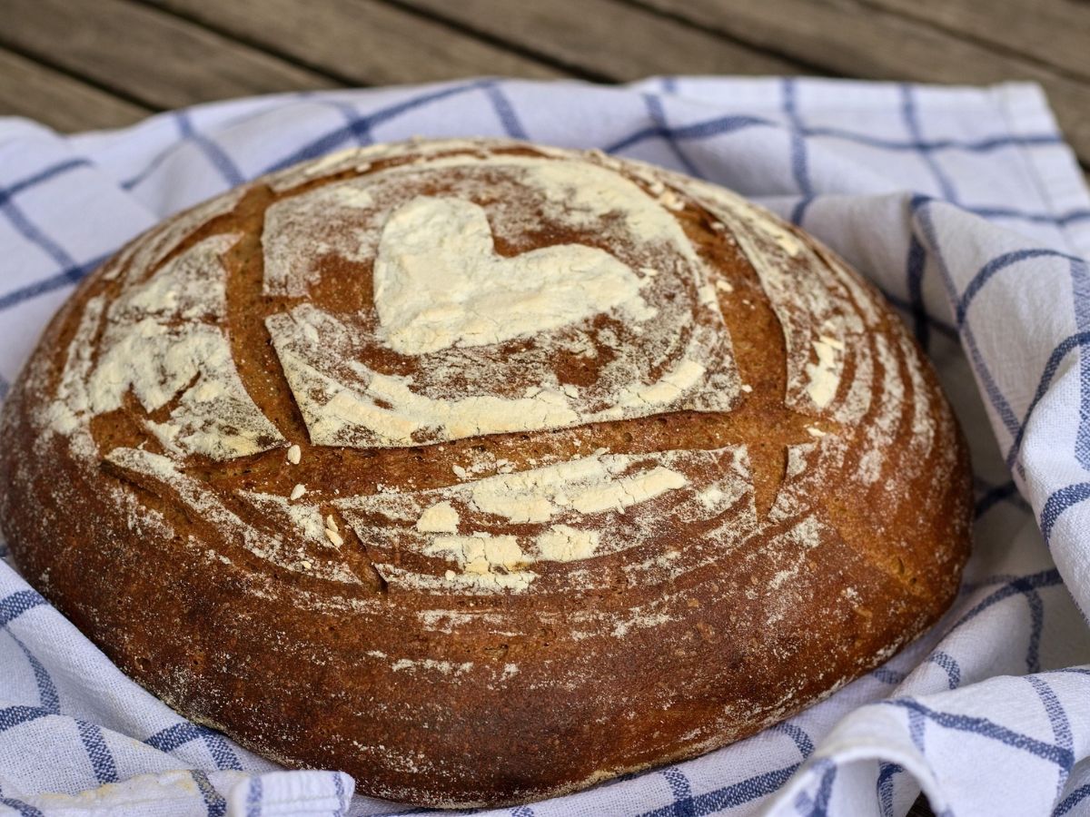 Round loaf of bread on a checkered cloth, with a heart shape made of flour on top.
