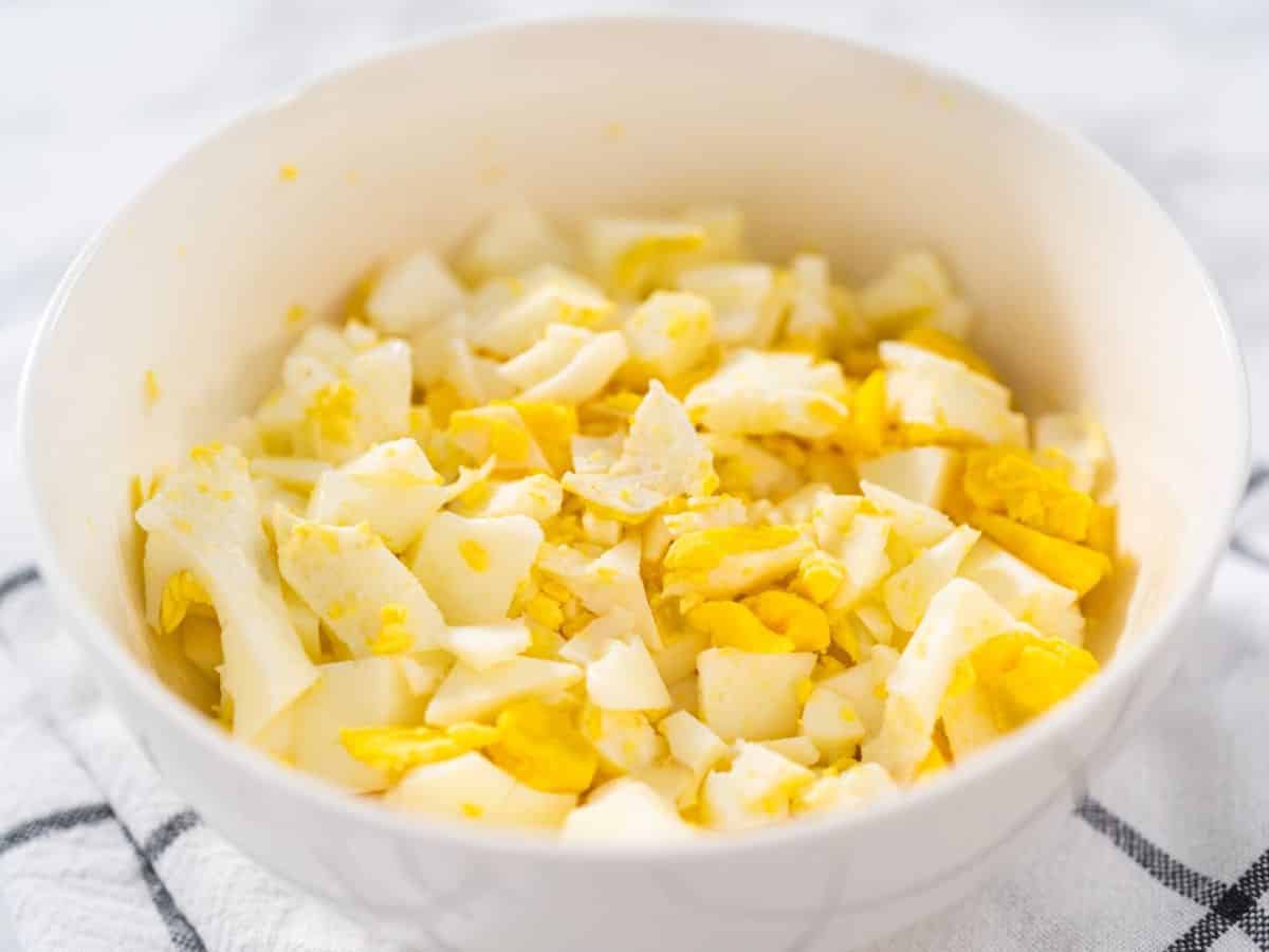 Chopped boiled eggs in a white bowl on a table.