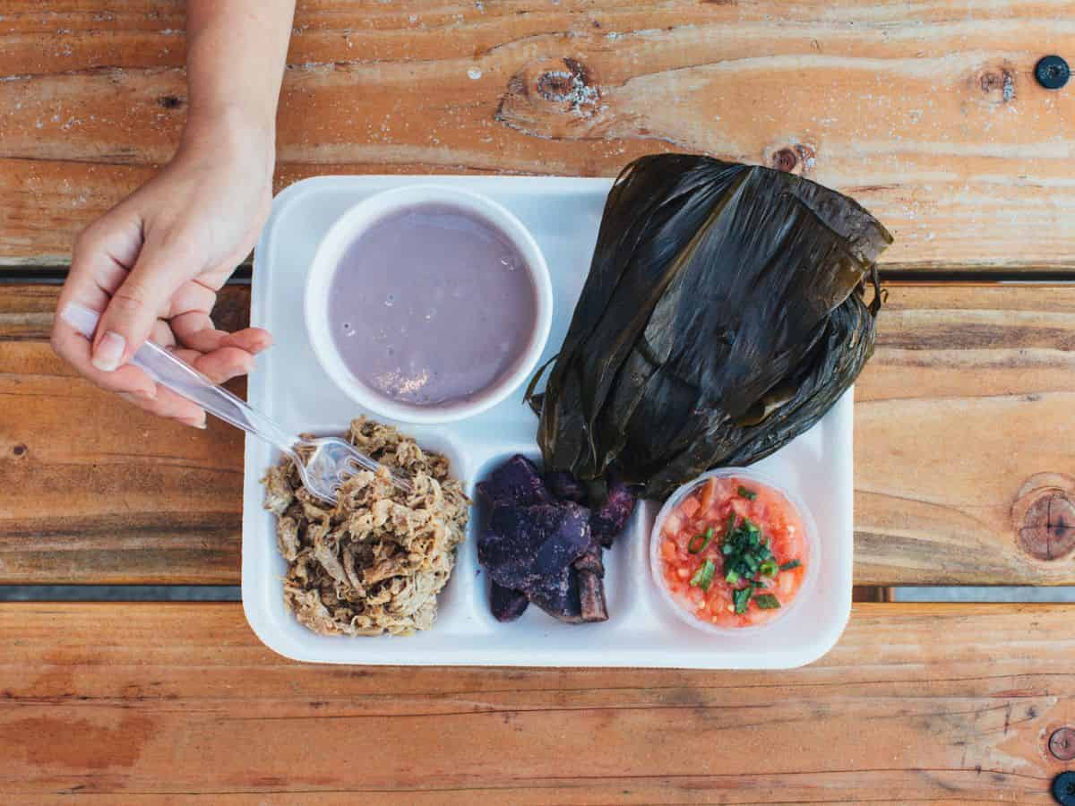 A woman eating a combination of traditional Hawaiian foods while seated at a wooden table.