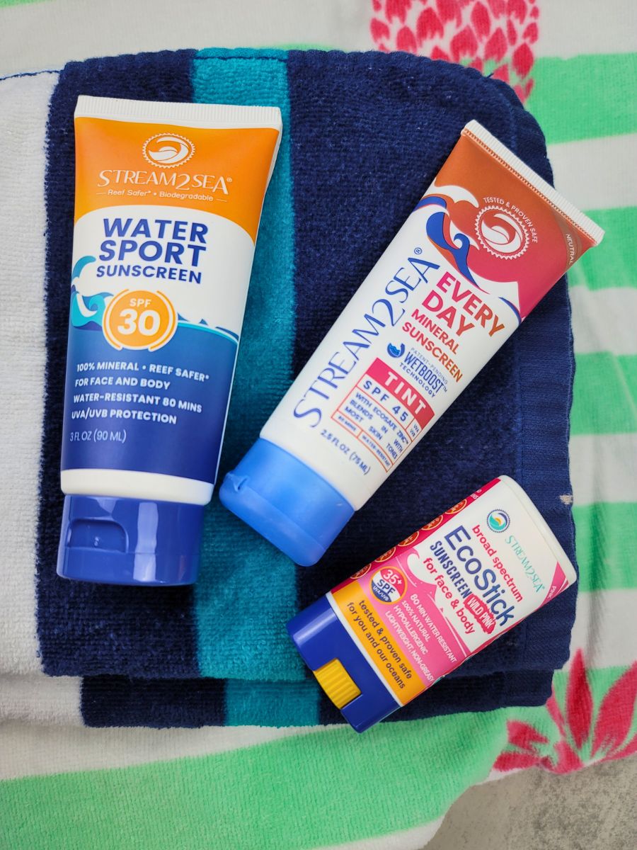 Three tubes of sunscreen by Stream2Sea on a striped towel: Water Sport Sunscreen SPF 30, Every Day Mineral Sunscreen SPF 45, and EcoStick SPF 35.