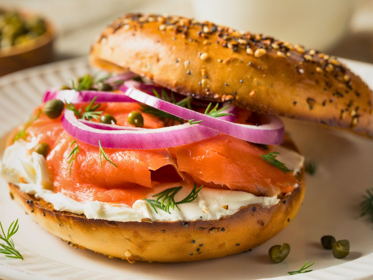 Bagel with cream cheese, smoked salmon, red onion slices, capers, and dill on a plate.