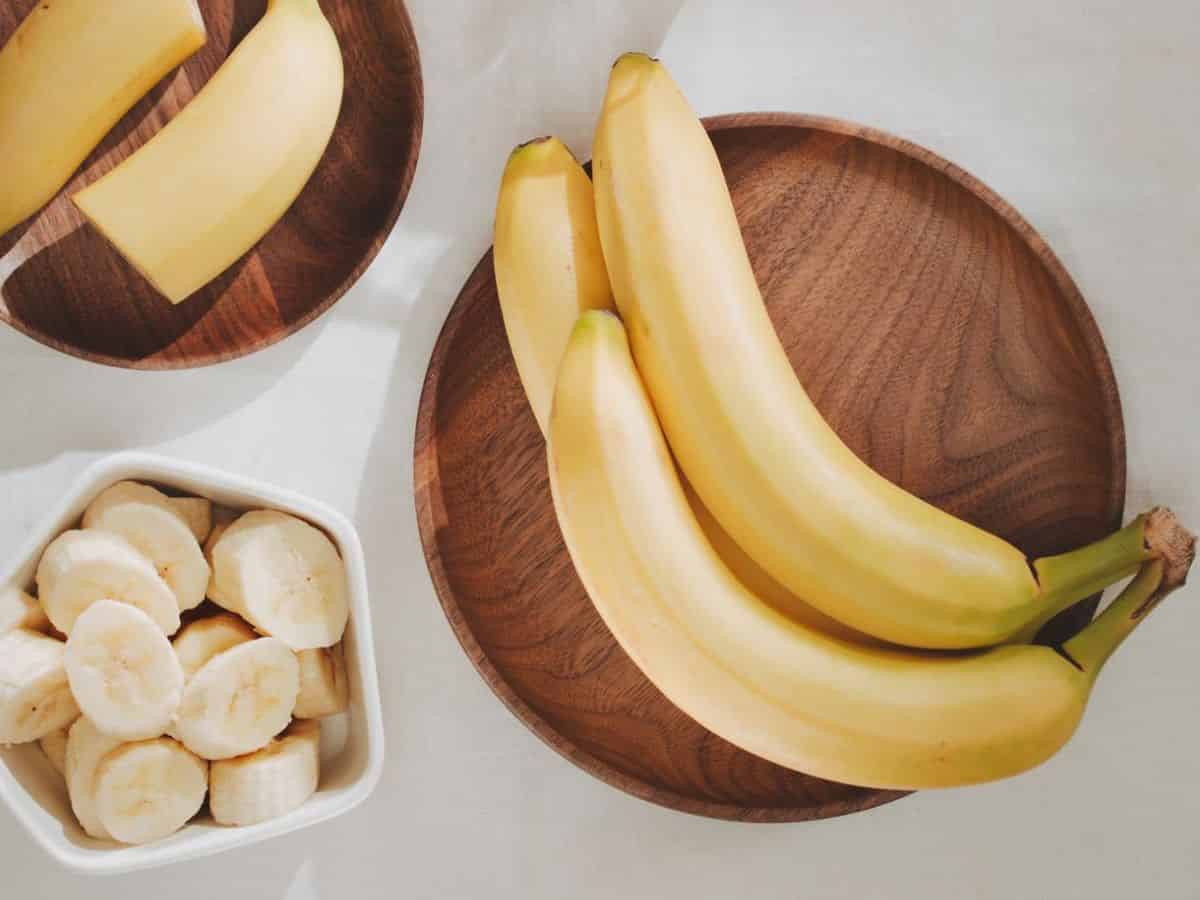 Bananas on a wooden plate with a bowl of sliced bananas.