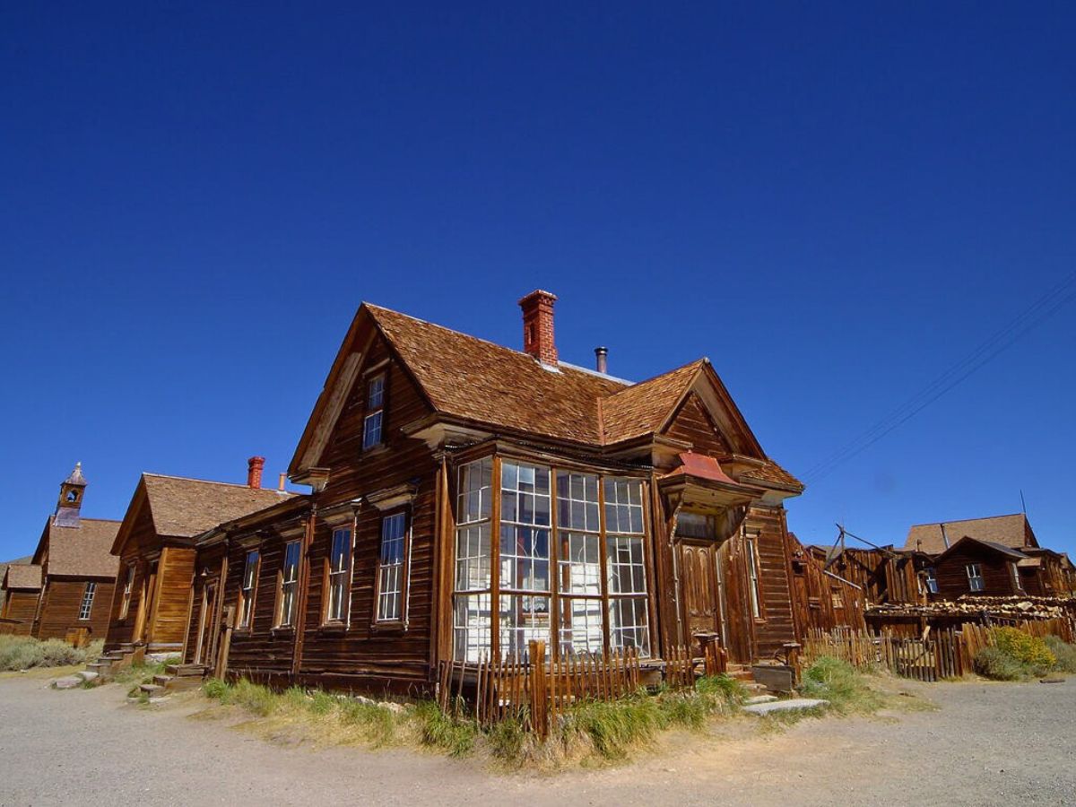 A rustic wooden house with a chimney in a deserted town under a clear blue sky.