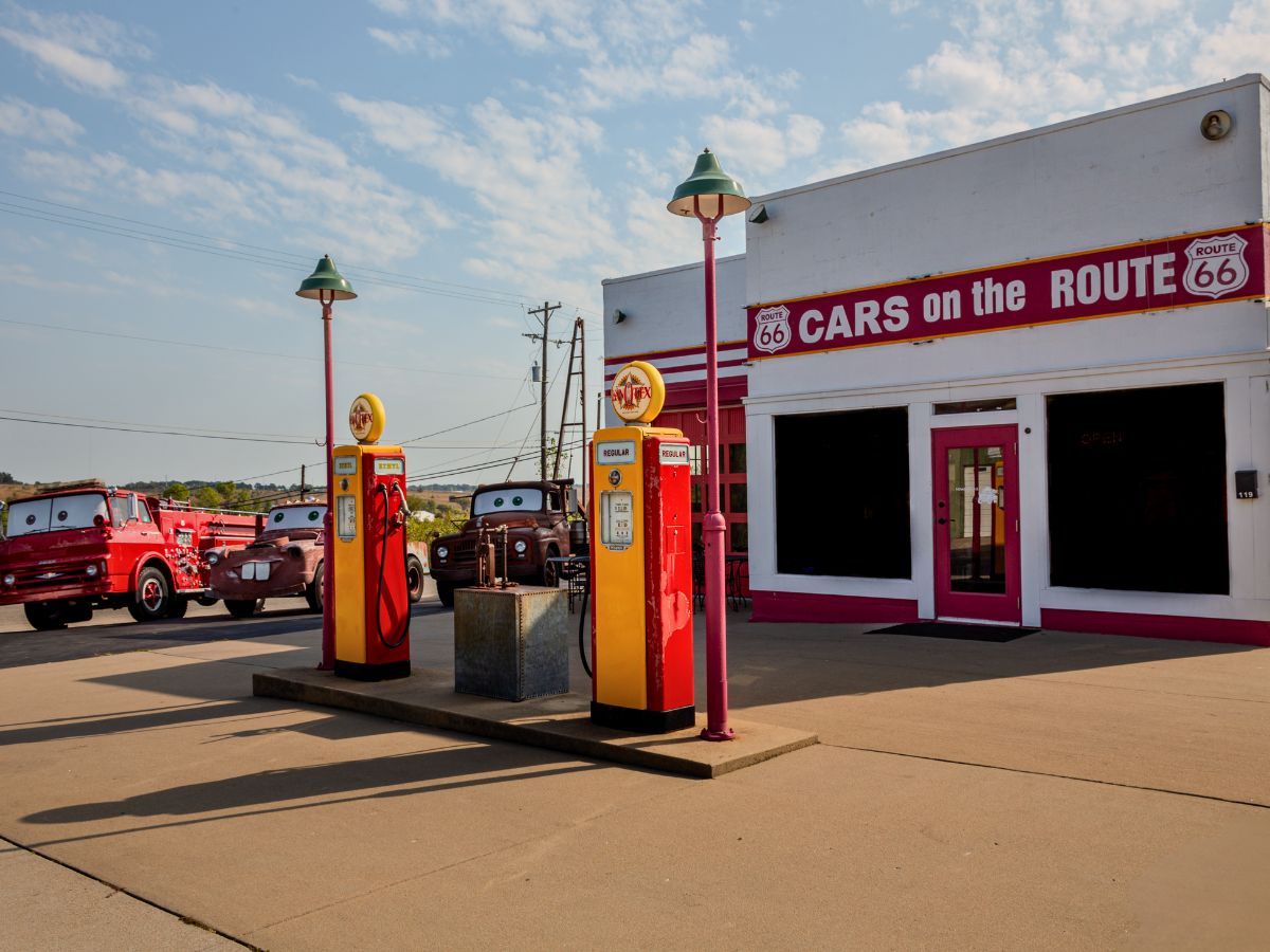 Retro gas station with vintage pumps and classic trucks in front of a building labeled "Cars on the Route" on Route 66.