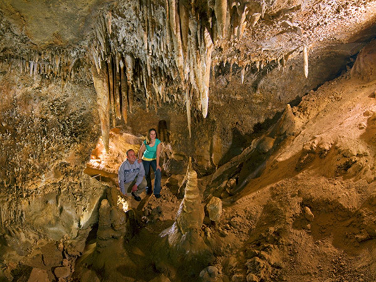 Two people explore a cave with stalactites and stalagmites surrounding them.