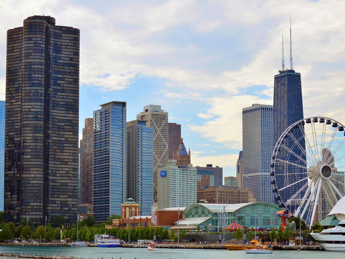 View of Chicago's skyline featuring various skyscrapers, a Ferris wheel by the waterfront, and a mix of modern and historic architecture against a partly cloudy sky.
