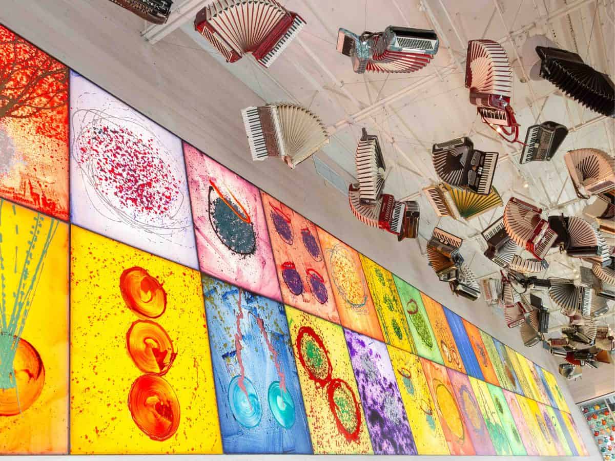 Chihuly's paintings on display in Seattle with his accordion collection hanging from the ceiling nearby.