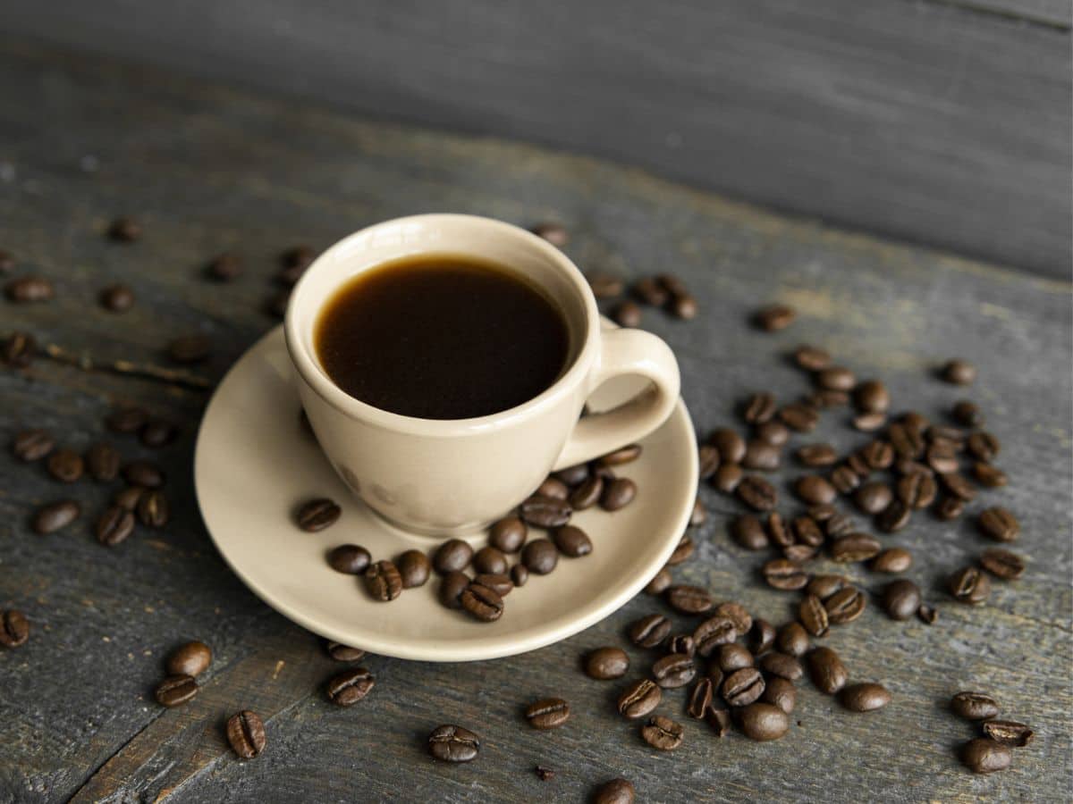 A cup of coffee with coffee beans on a wooden table.