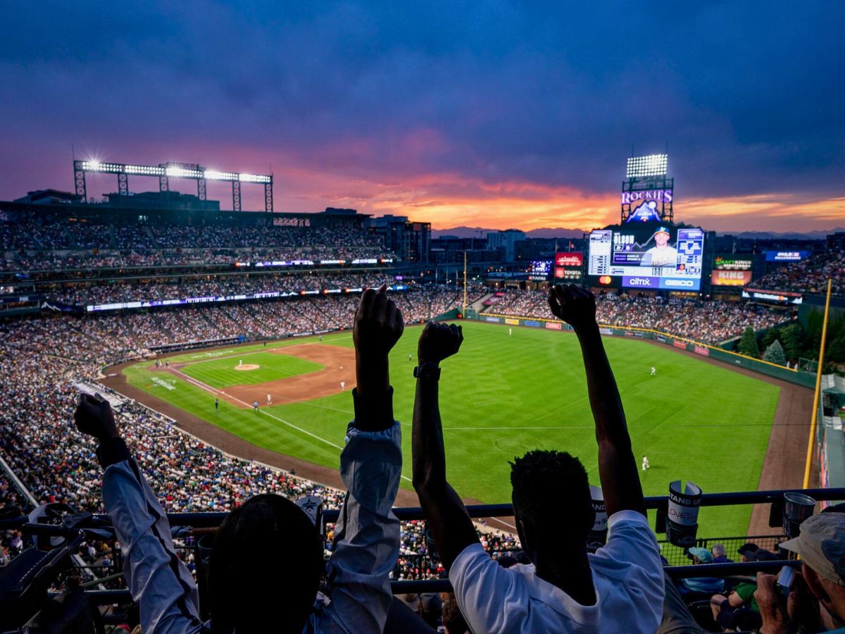 Fans cheer at a baseball game in a crowded stadium during sunset.