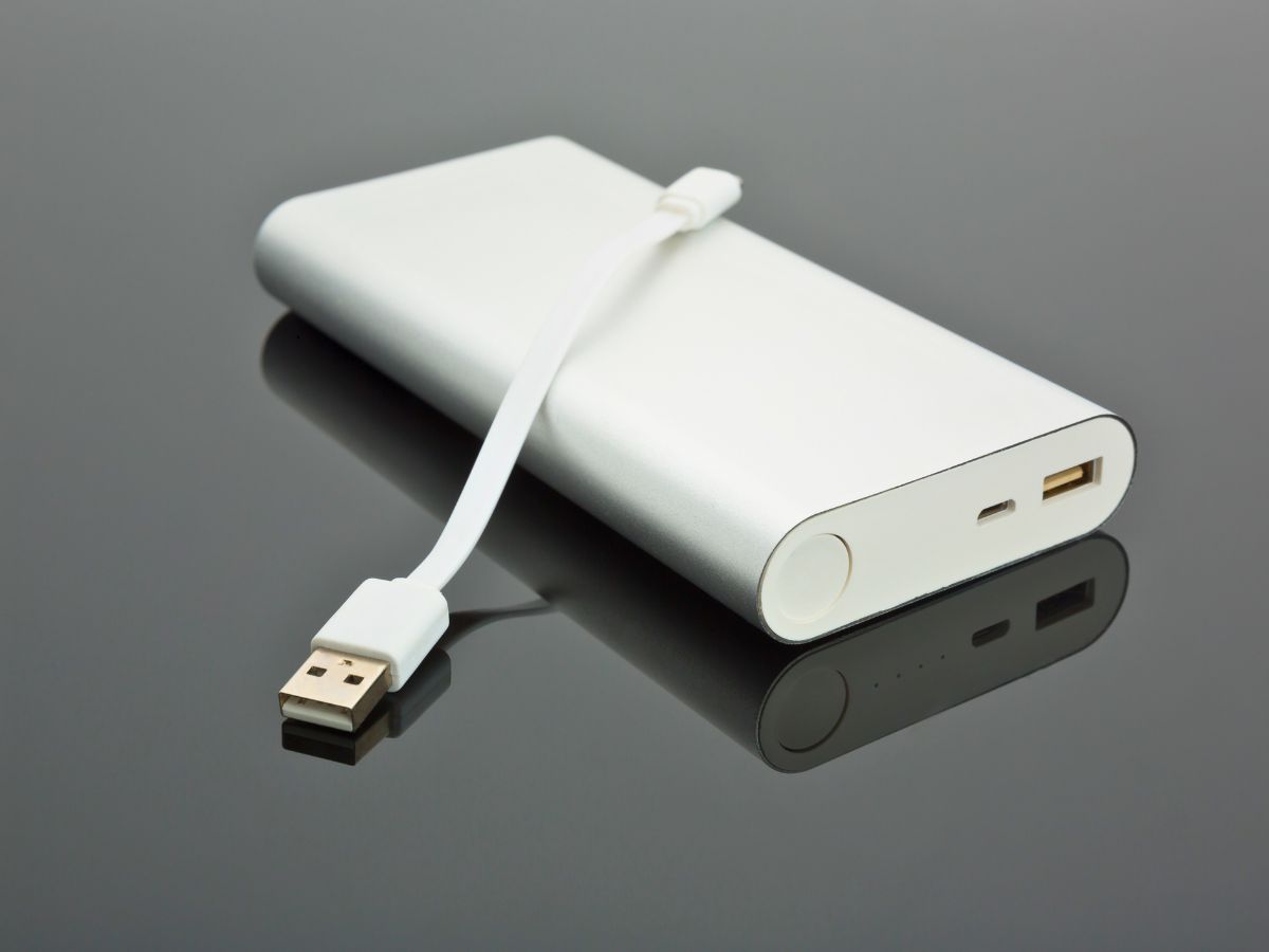 A white power bank with a USB cable attached lies on a glossy dark surface.