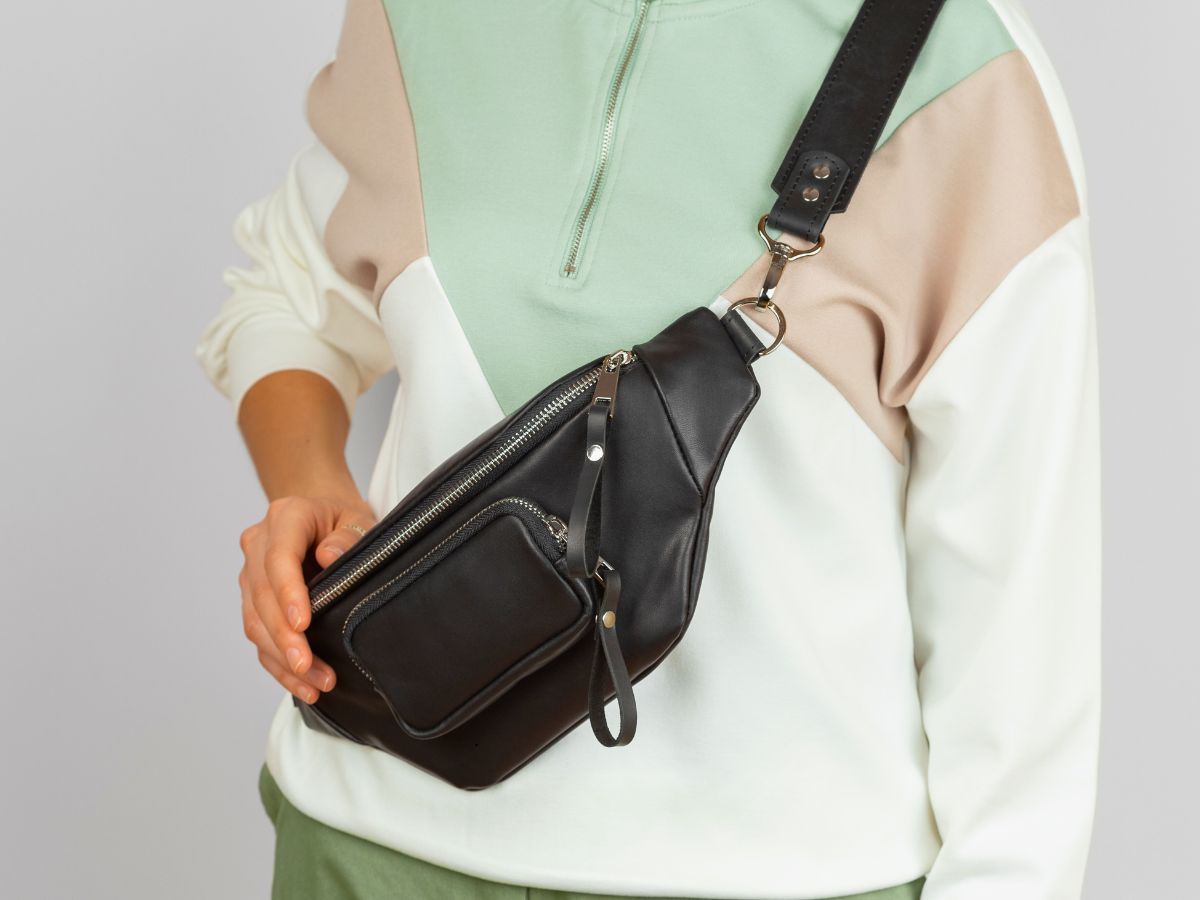 Person wearing a color-blocked sweatshirt and holding a black crossbody bag with multiple zippers.