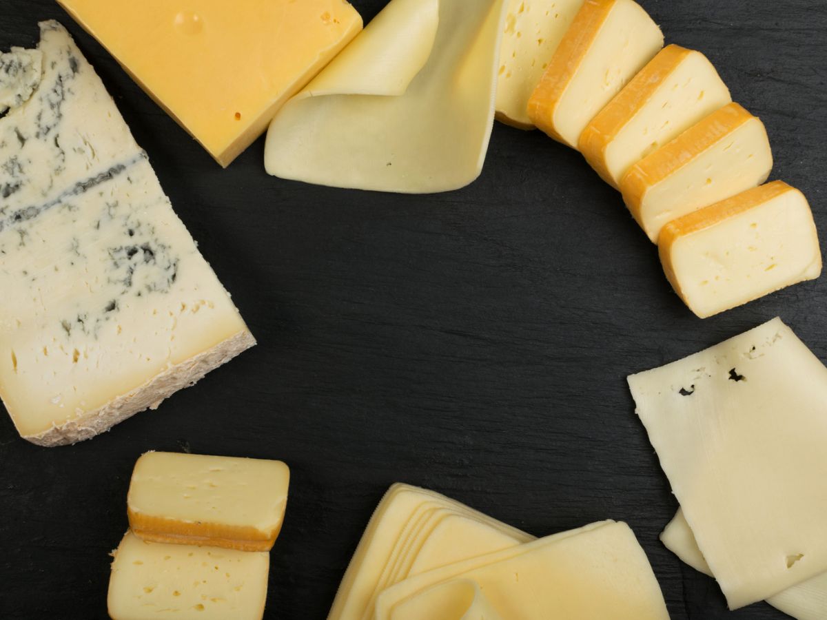 Various sliced and whole pieces of cheese arranged in a circular pattern on a black surface.