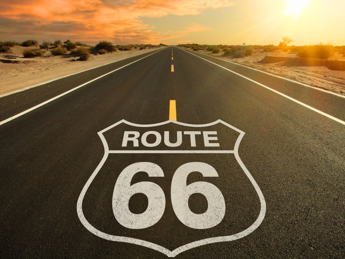 Straight view of Route 66 in a desert landscape at sunset, with the iconic highway shield symbol painted on the asphalt.