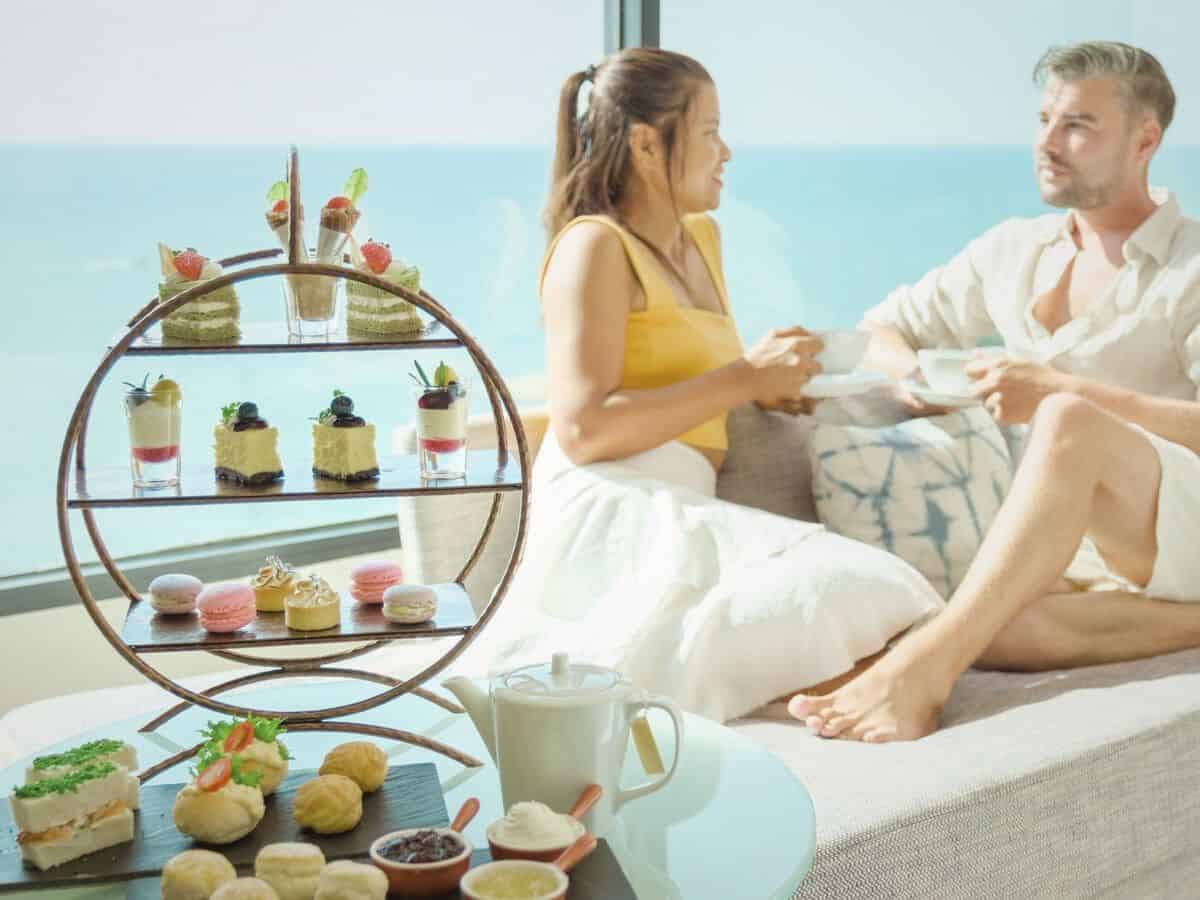 A man and woman sitting on a couch enjoying afternoon tea.