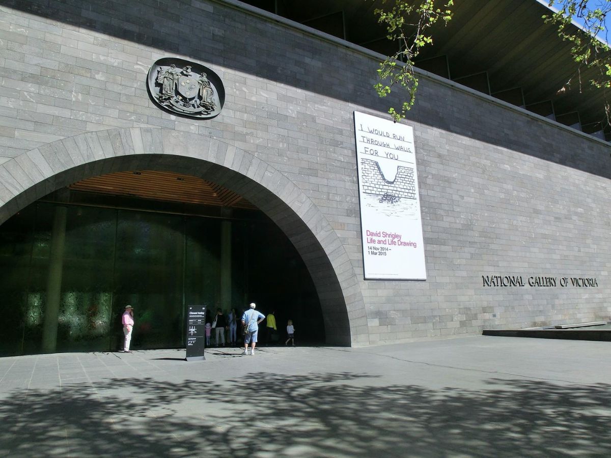 The front entrance of the National Gallery of Victoria, featuring a large arched doorway and a poster advertising an art exhibition.