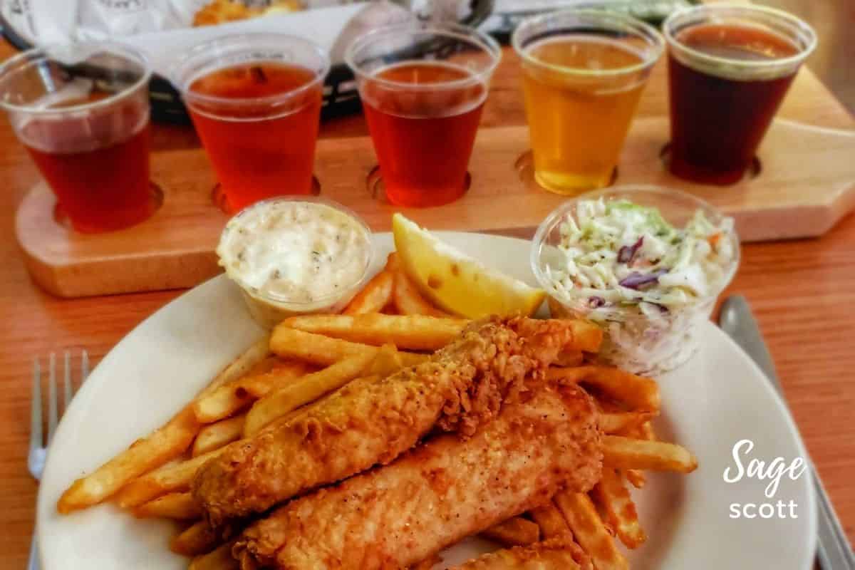 A plate of fish and chips and beer on a wooden table.