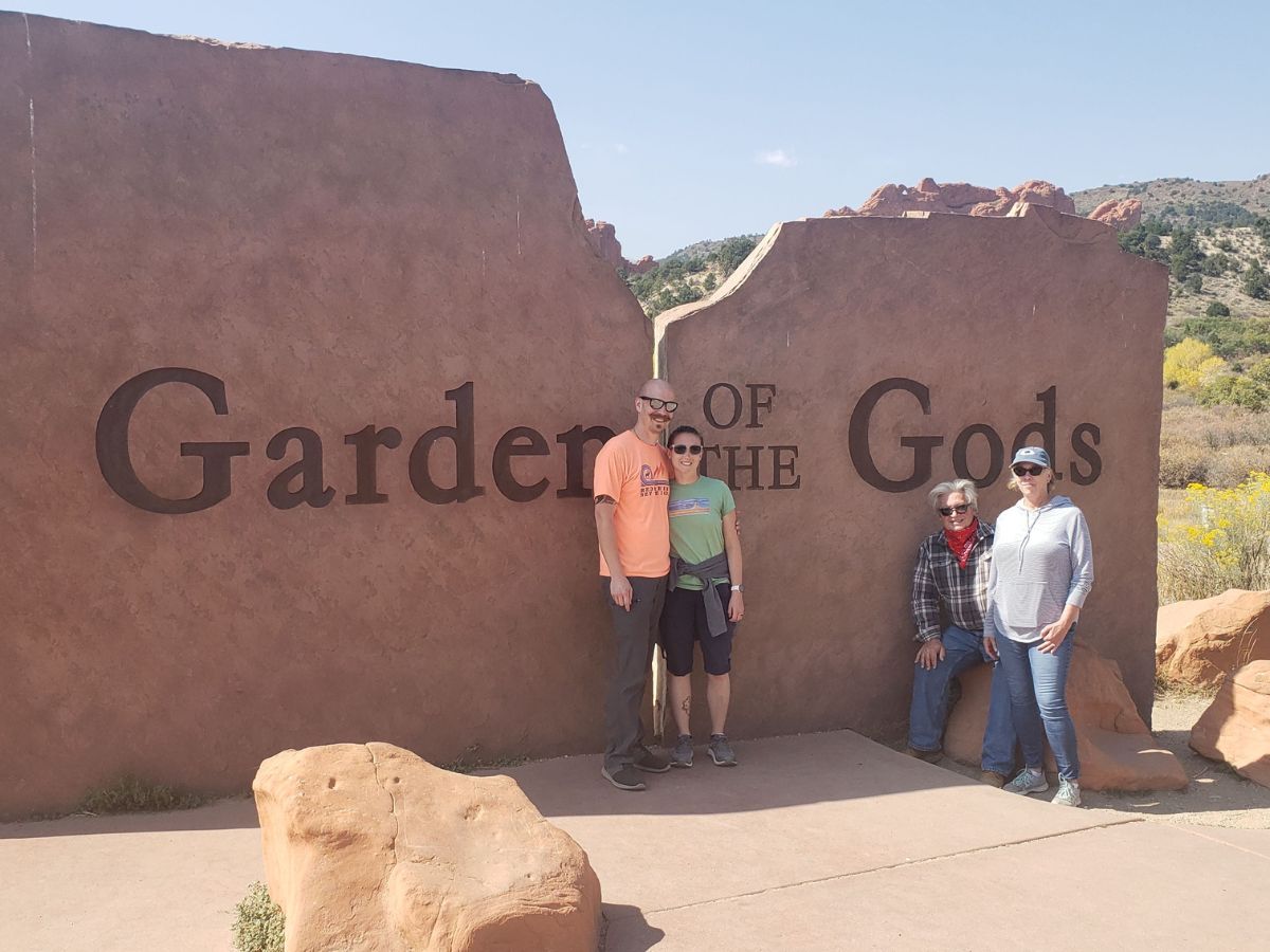 Four people stand in front of the "Garden of the Gods" sign with a desert landscape in the background.