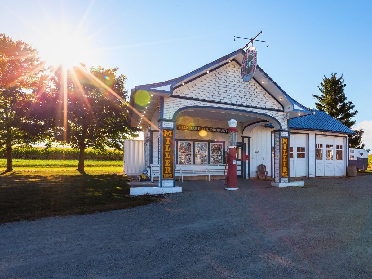Historic gas station with a "Standard Oil Products" sign, surrounded by trees and a bright sunburst in the background.