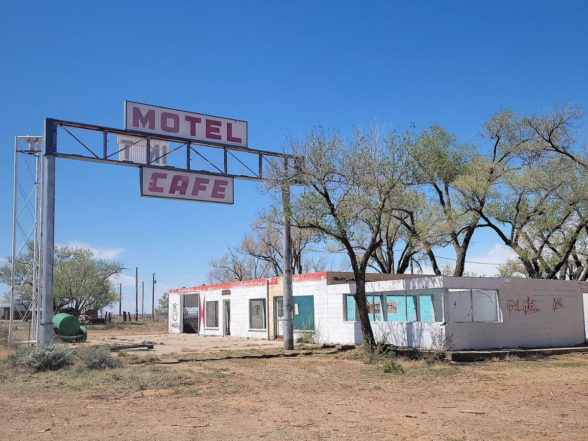 An abandoned motel and cafe with faded signs, surrounded by trees and a clear blue sky.