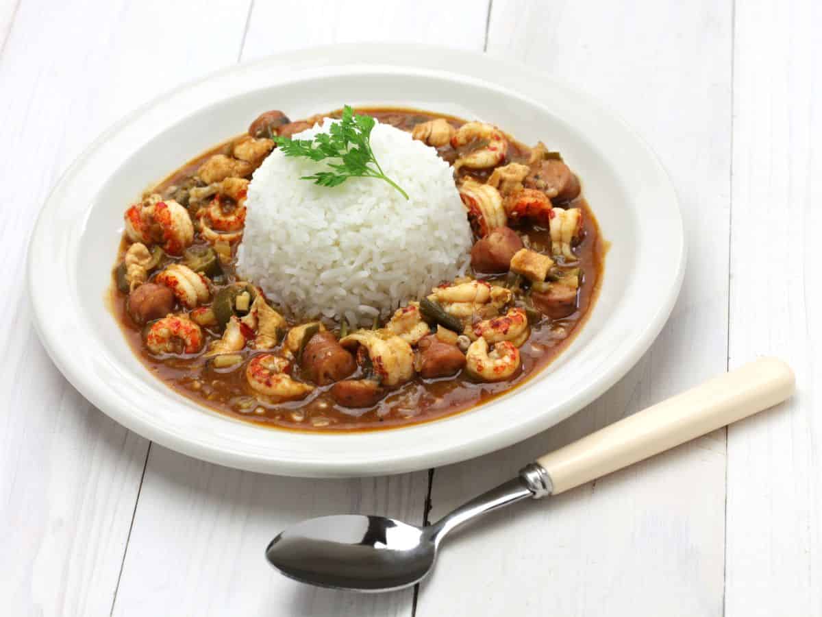 A white bowl of gumbo and rice on a wooden table.