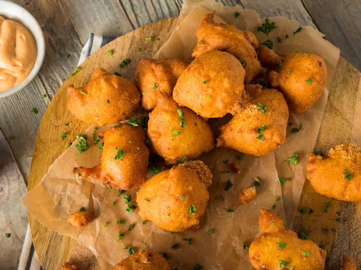 Hush puppies on brown parchment paper on a wooden board with dipping sauce.