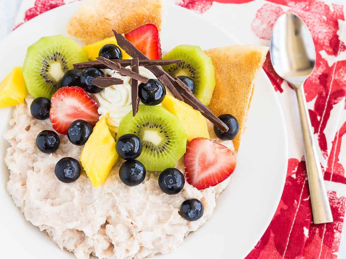 A bowl of kulolo topped with fruit and served with a spoon is a popular luau food.