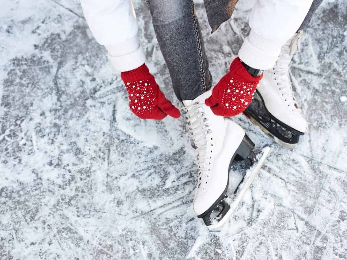 Woman sitting on the ice tying the laces of white ice skates
