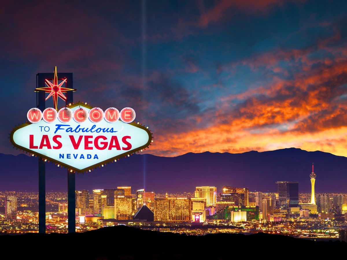 The iconic "Welcome to Fabulous Las Vegas, Nevada" sign with the city skyline and a colorful sunset in the background.