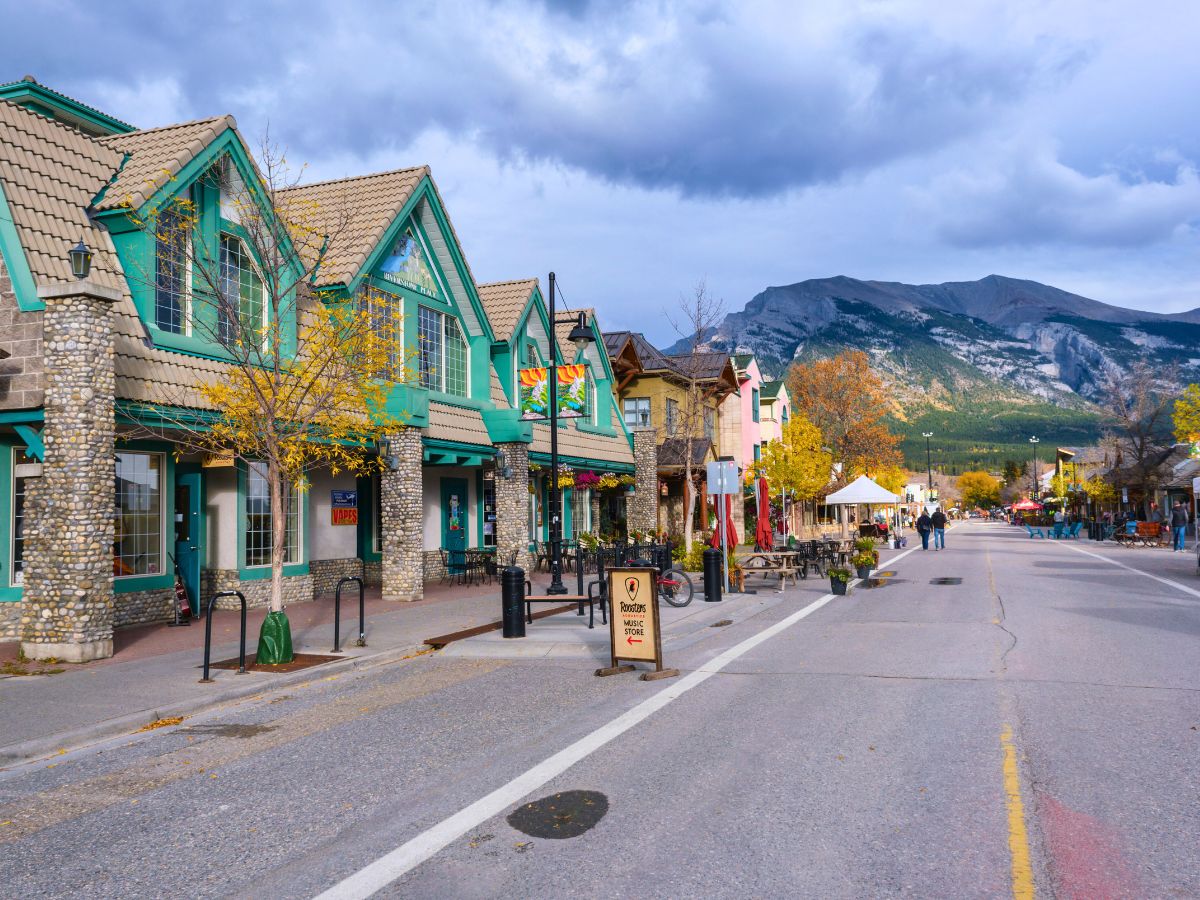 Small town street with colorful buildings on a cloudy day, mountains in the background, and people walking.