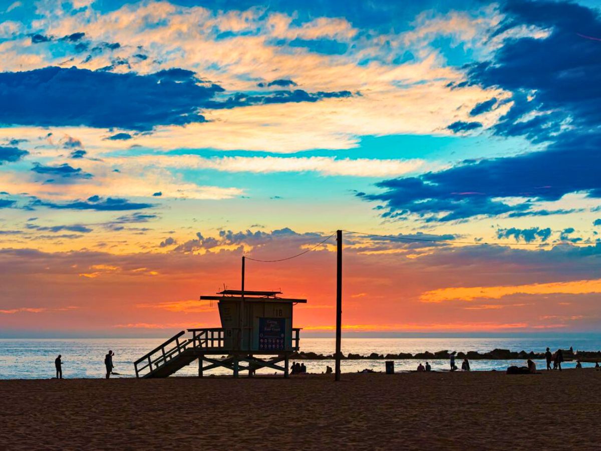 Sunset at a beach with silhouette of a lifeguard station and people enjoying the evening.