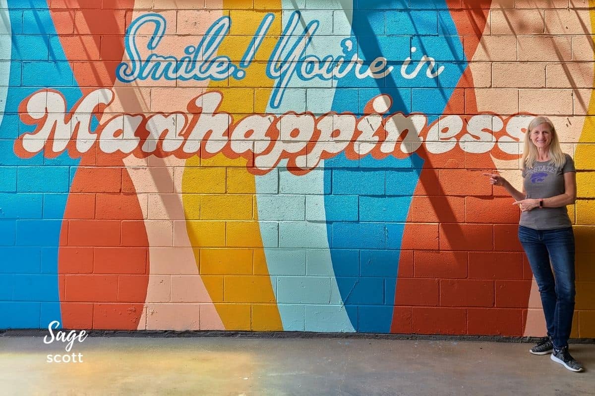 Sage standing in front of the colorful "Smile You're in Manhappiness" mural in Manhattan KS