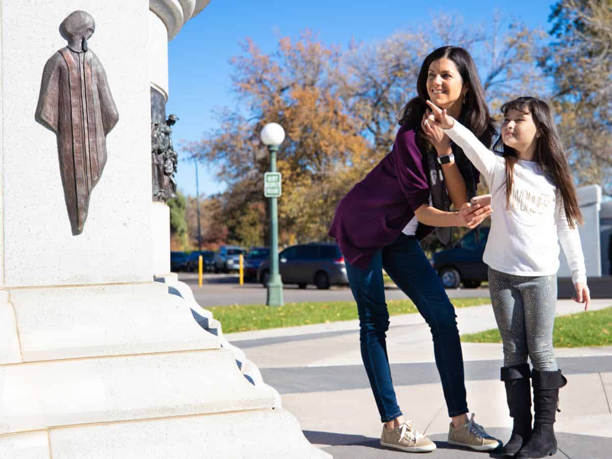 A woman and her daughter on a scavenger hunt, standing next to a statue.