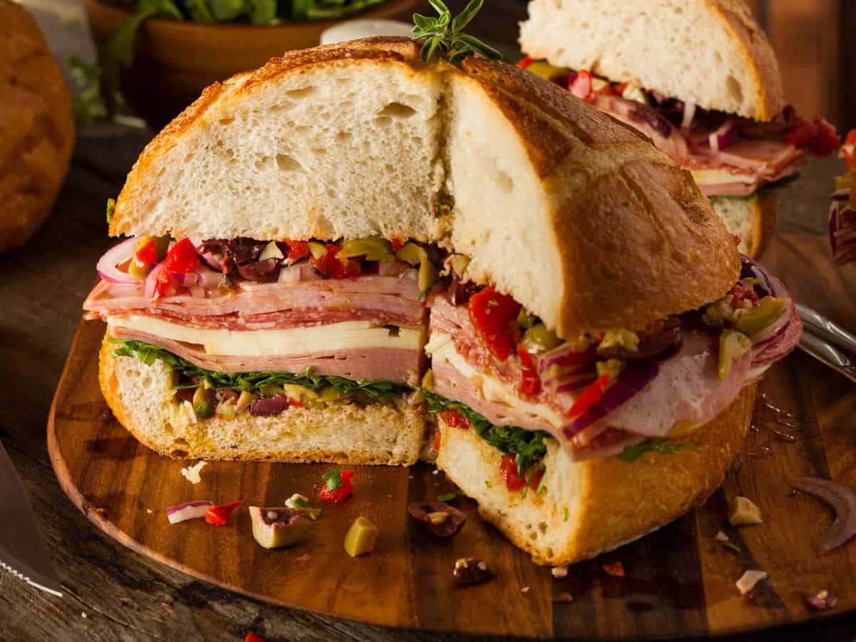 A muffuletta sandwich cut in half on a wooden cutting board.