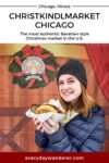 A smiling person in a winter outfit holds a sandwich in front of a Christkindlmarket Chicago sign with a wreath.