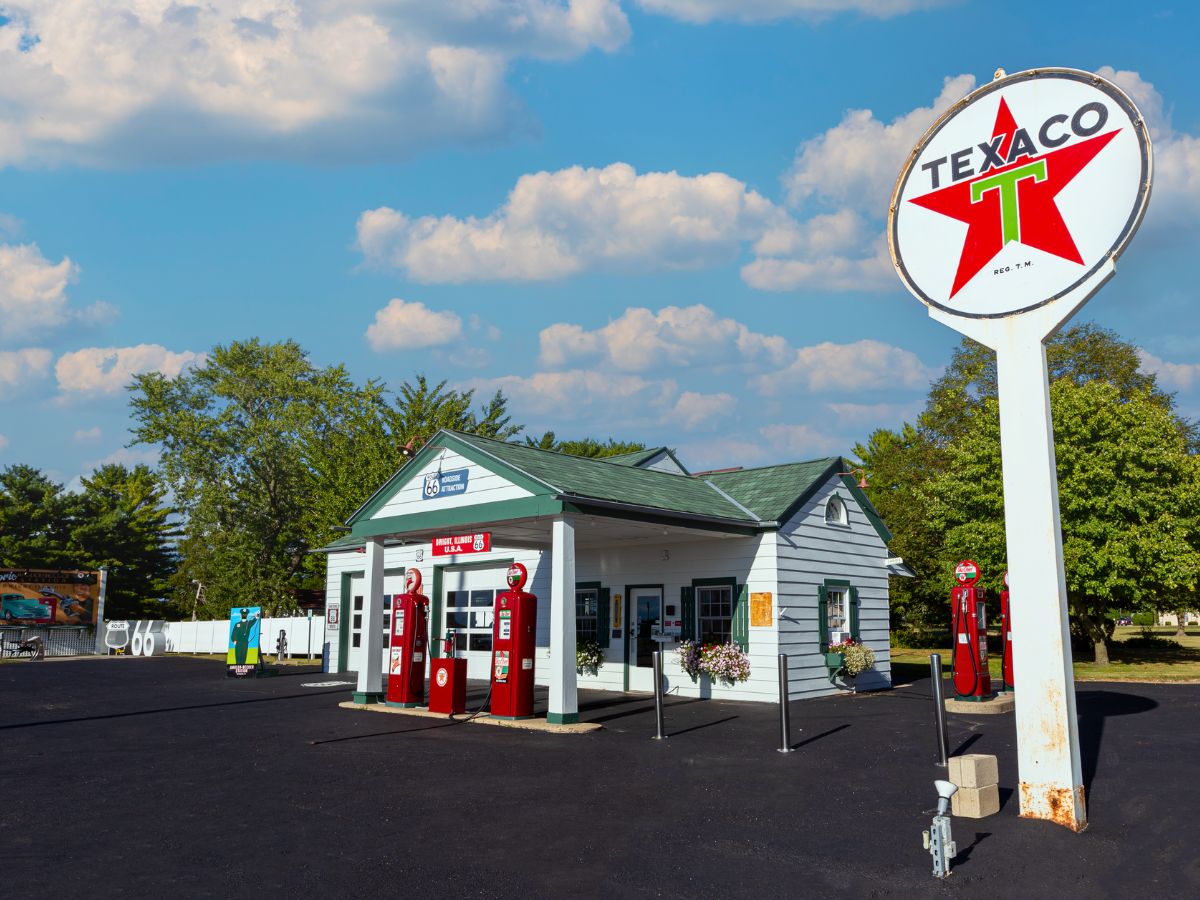 Vintage Texaco gas station with red pumps, set against a backdrop of trees and a blue sky with clouds.