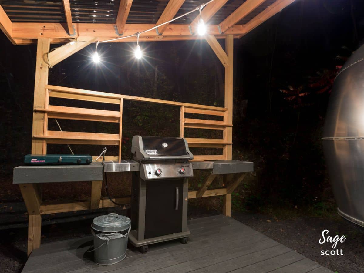 A wooden deck attached to an Airstream with a barbeque grill.
