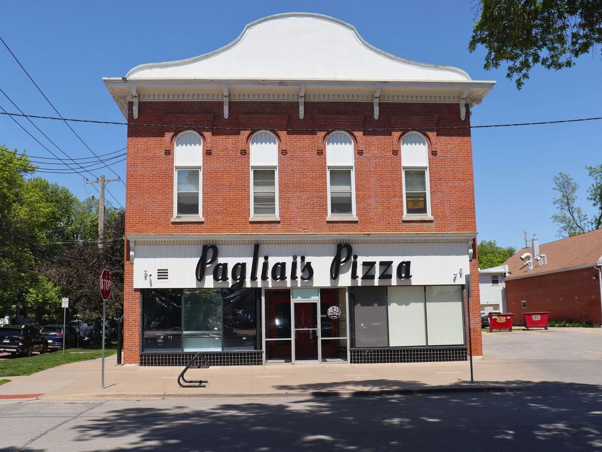 A two-story brick building with an awning sign reading "Pagliai's Pizza" and several large windows on the ground floor, located on a sunny street corner.