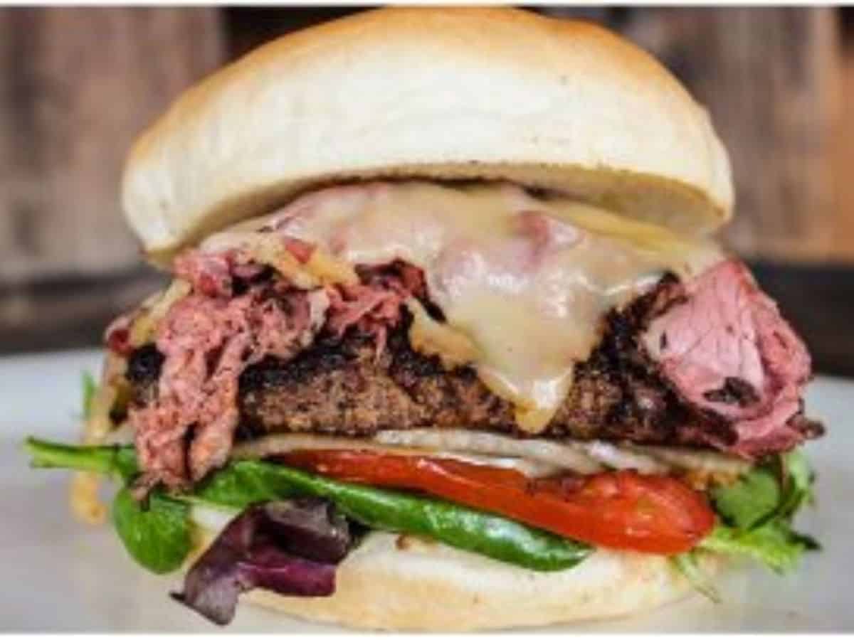 A pastrami burger plated with lettuce and tomatoes.