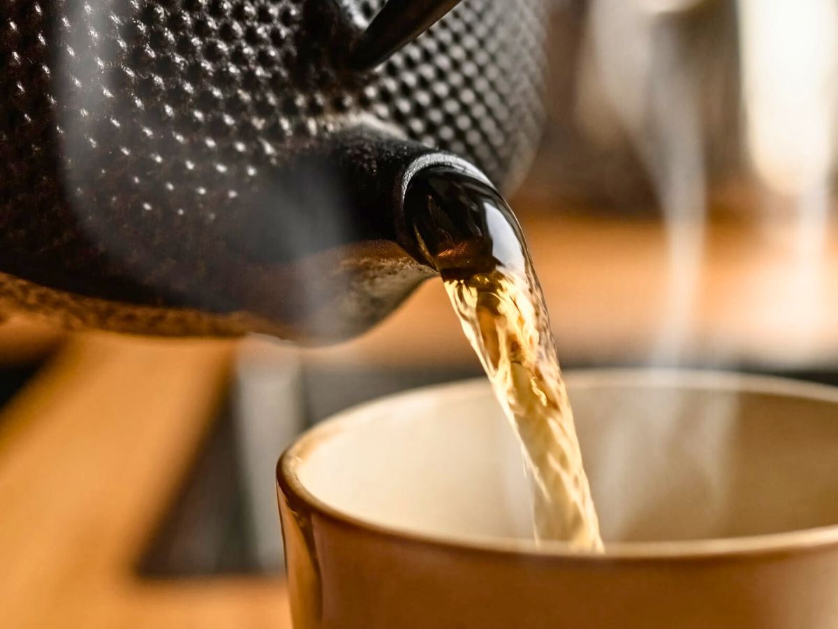 Pouring hot tea from a teapot into a cup.