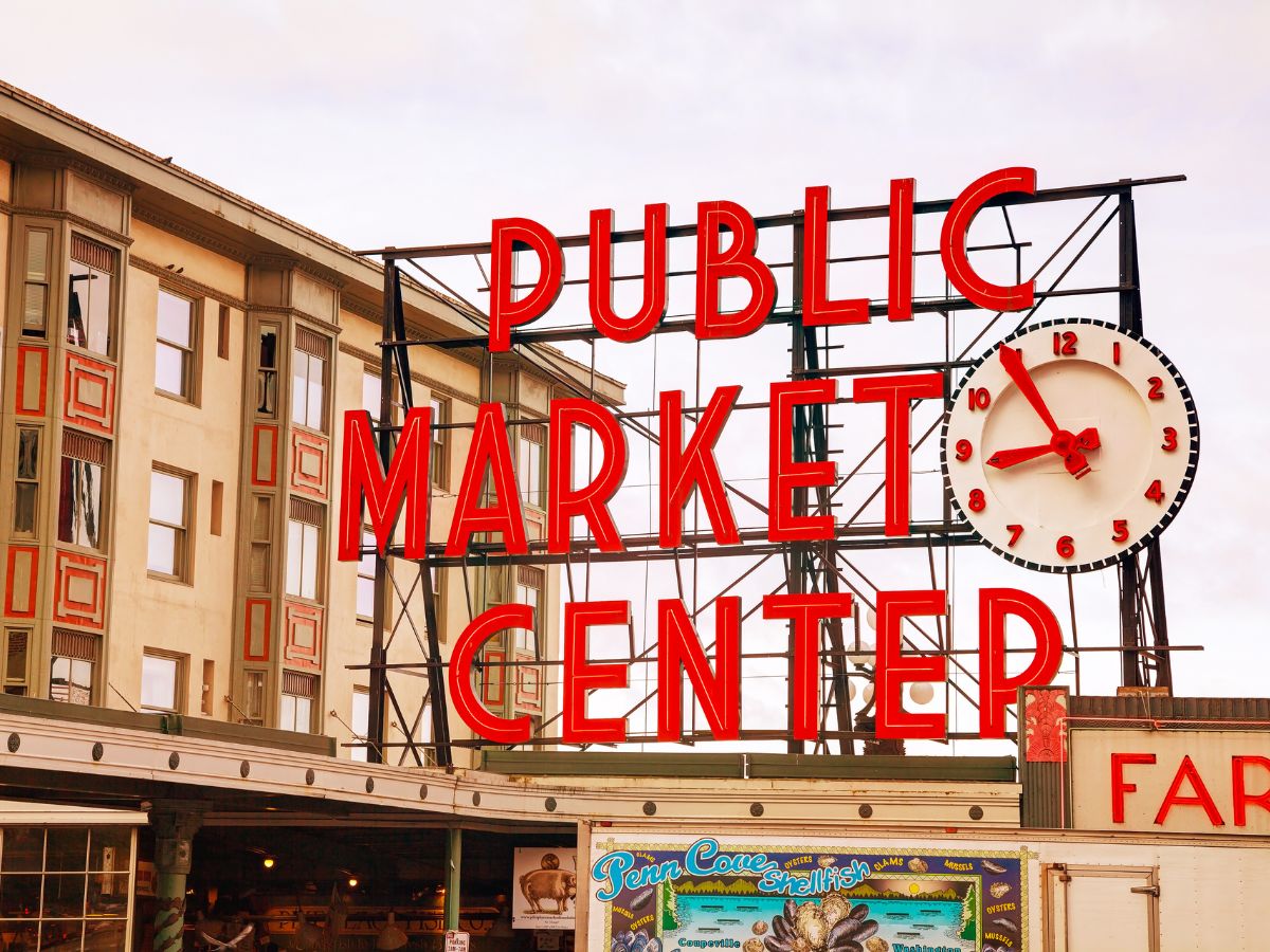 Public Market Center sign with a red clock on a building facade, featuring a fish market stall in the foreground.