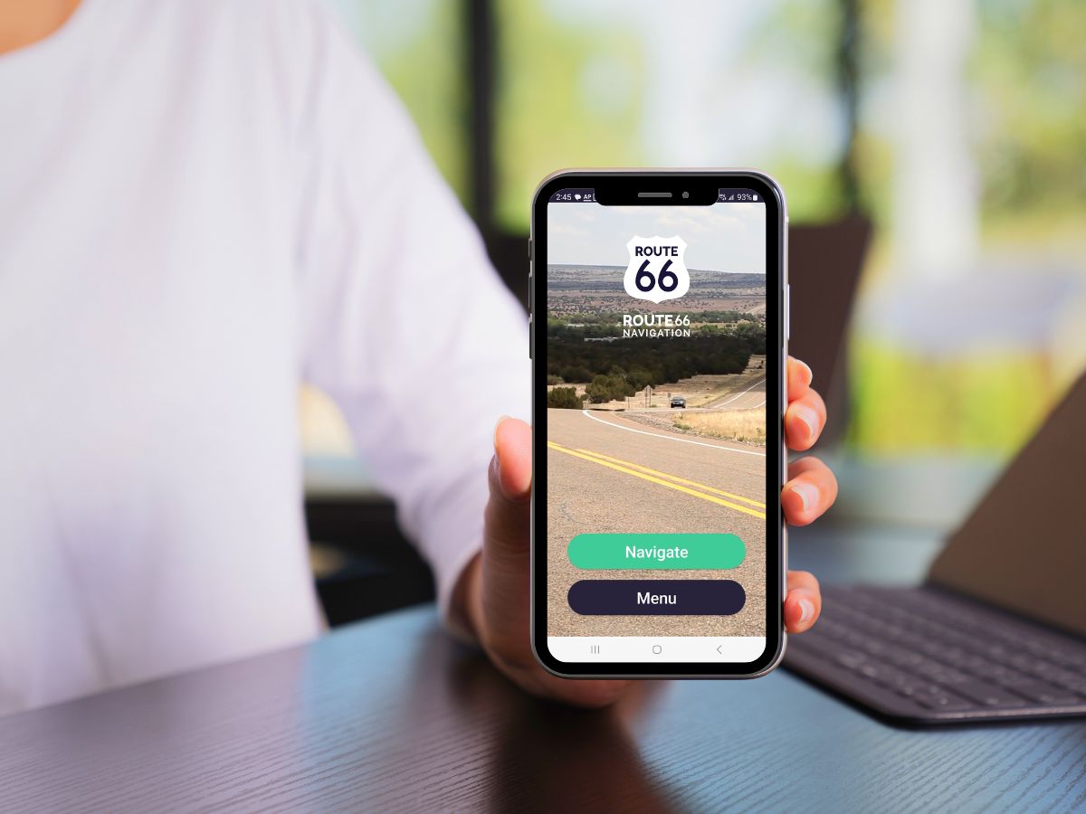 Person holding a smartphone displaying a Route 66 navigation app with "Navigate" and "Menu" buttons.