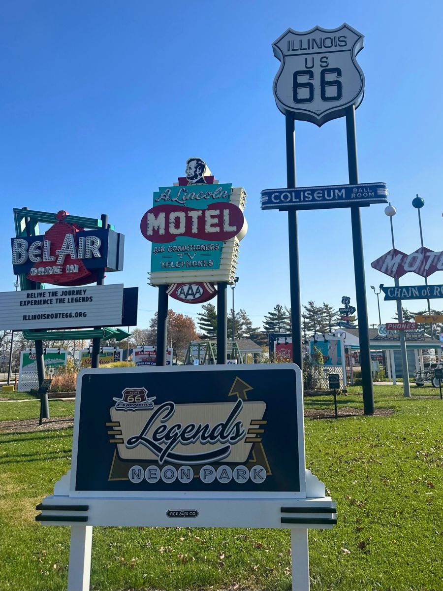 A display of retro motel signs at Legends Neon Park, featuring Illinois Route 66 signage and the Lincolns Motel sign in a grassy area.