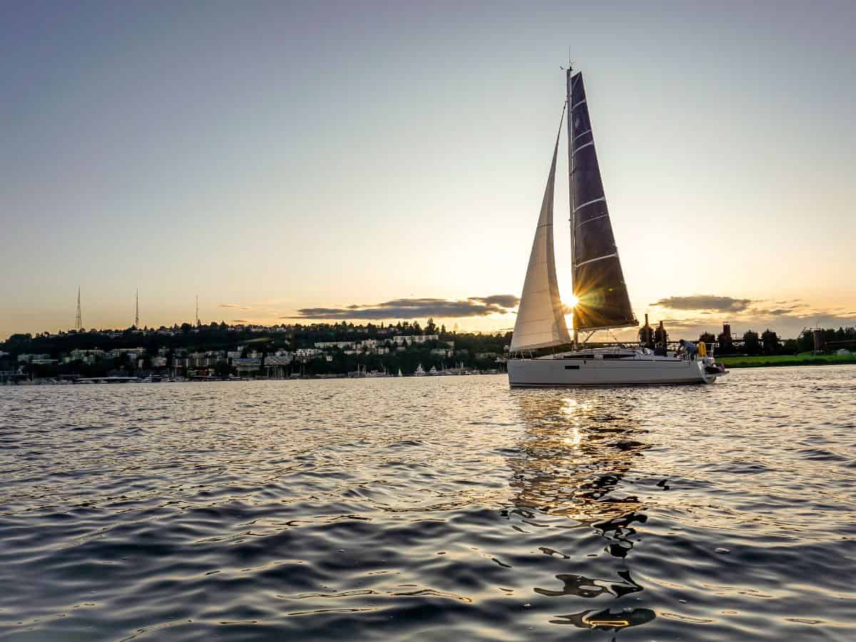A sailboat sails on Lake Union at sunset.