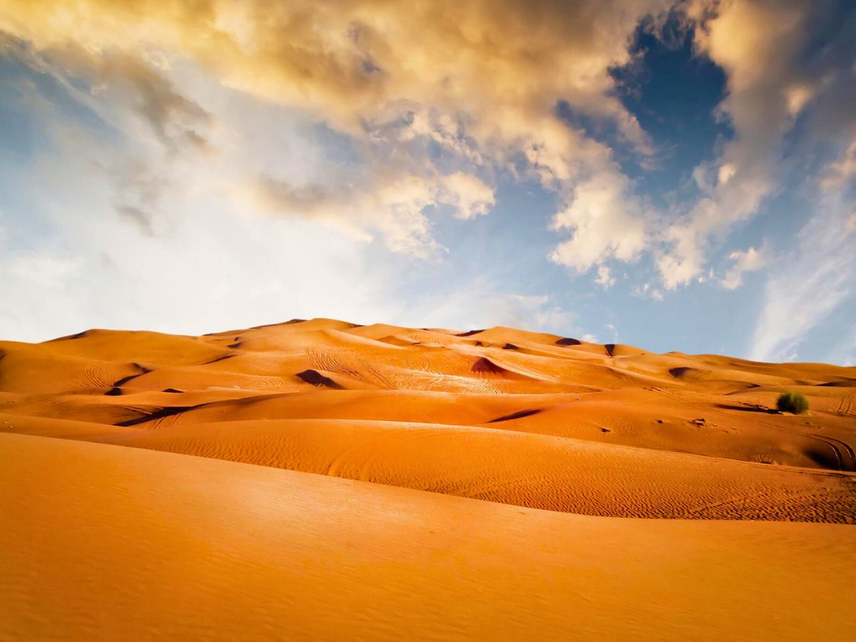 Undulating sand dunes under a dynamic sky at sunset.
