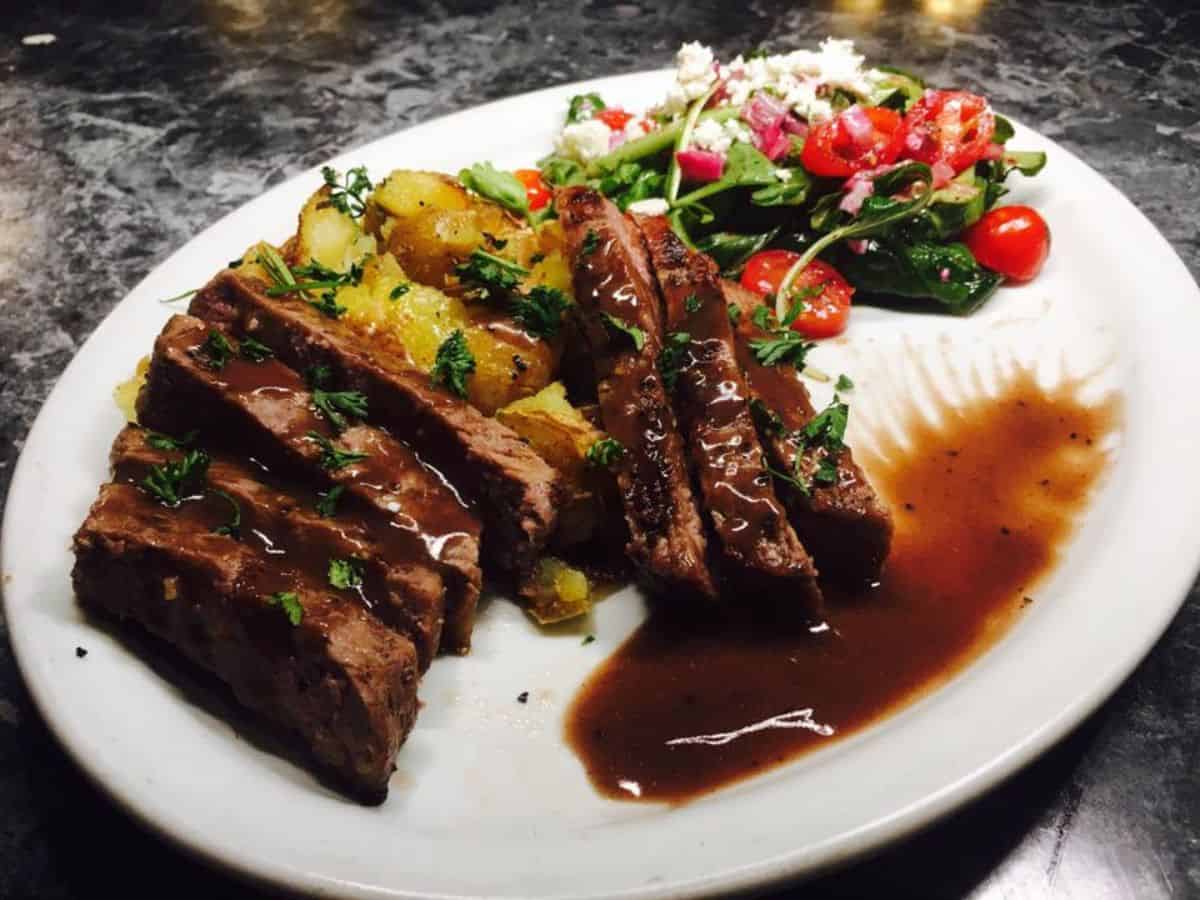 A strip steak topped with Bordelaise sauce next to a side of smashed potatoes.