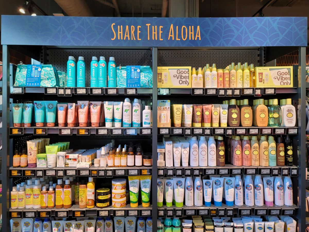 Store shelf display of various skincare and sunscreen products, packed tightly in an organized manner with a sign reading "Share The Aloha" at the top.