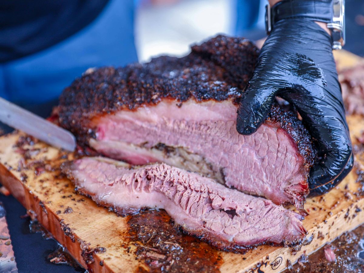 A gloved hand slicing smoked brisket on a wooden cutting board.