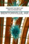 Indoor blue spiked sculpture hanging from the ceiling of a building with wooden beams, accompanied by text promoting Bentonville, AR, as a destination for art and outdoor activities.