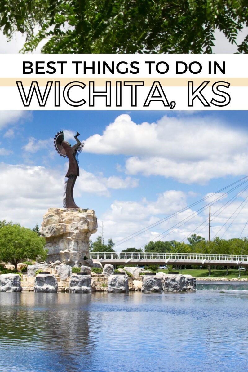 A statue of a Native American figure stands atop a rock formation by a river, with a footbridge and green trees visible in the background. The text above reads, "Best Things to Do in Wichita, KS.