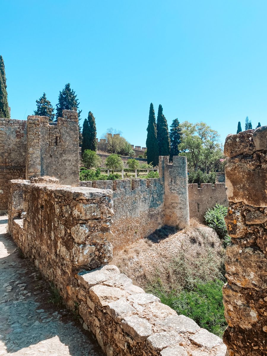 A stone fortress with tall, tree-lined walls and a clear blue sky in the background.